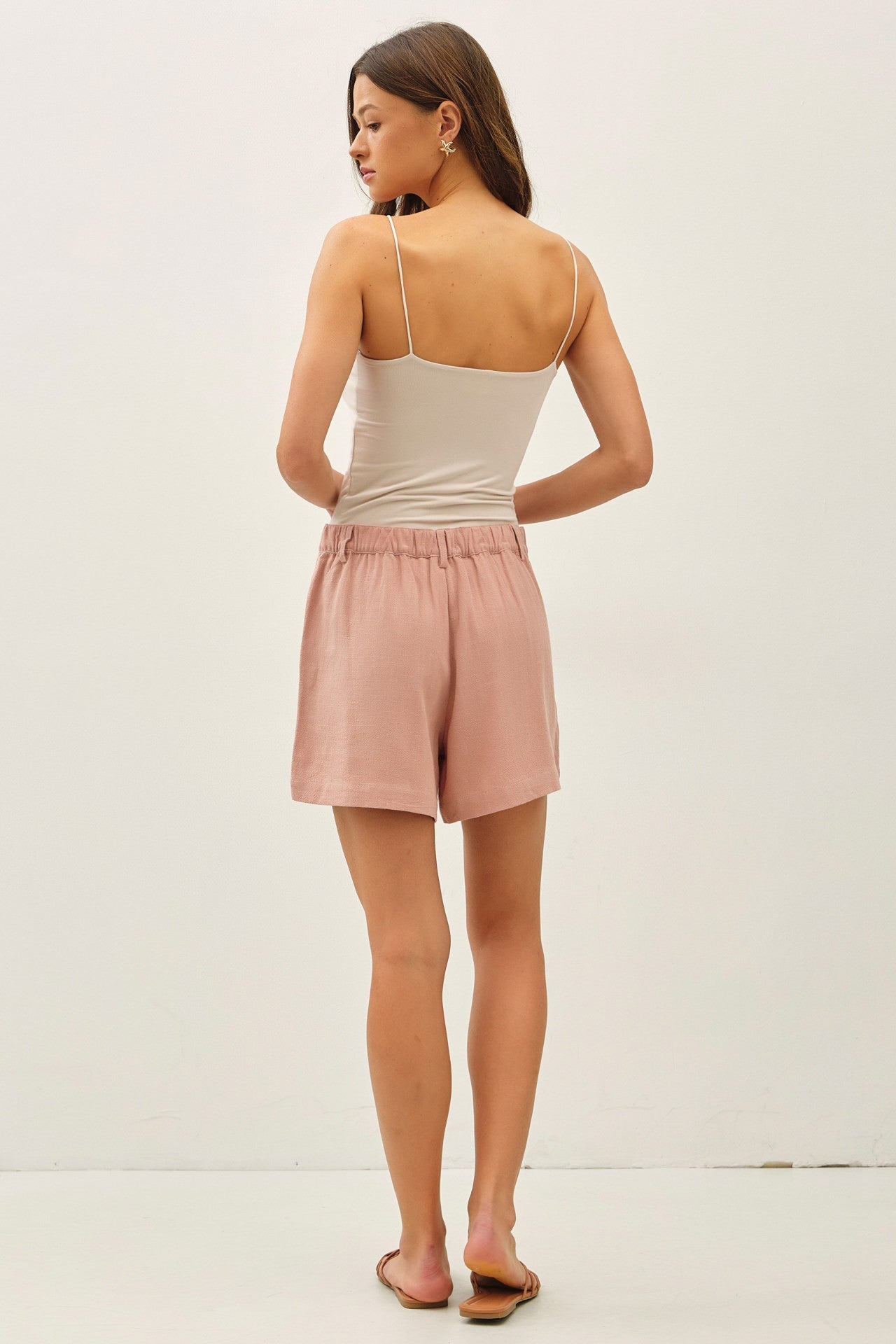 woman wearing a plain white spaghetti strap top and light pink shorts, facing away from the camera
