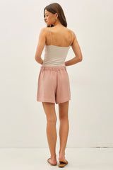 woman wearing a plain white spaghetti strap top and light pink shorts, facing away from the camera