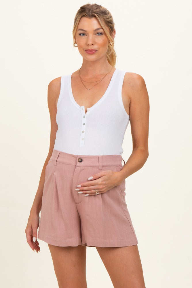woman wearing a white ribbed maternity tank top and pink high-waisted shorts, showing her baby bump