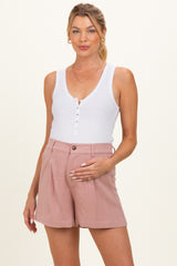 woman wearing a white ribbed maternity tank top and pink high-waisted shorts, showing her baby bump