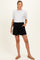 woman wearing a white short sleeve top and black maternity shorts, standing with hands in pockets