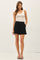 woman wearing a cream tank top and high-waisted black shorts with a button detail