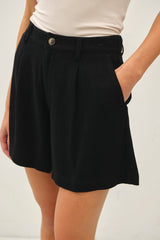 woman wearing high-waisted black pleated shorts with a side pocket detail