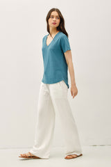 woman wearing a teal v-neck t-shirt and white wide-legged pants, walking in a relaxed pose