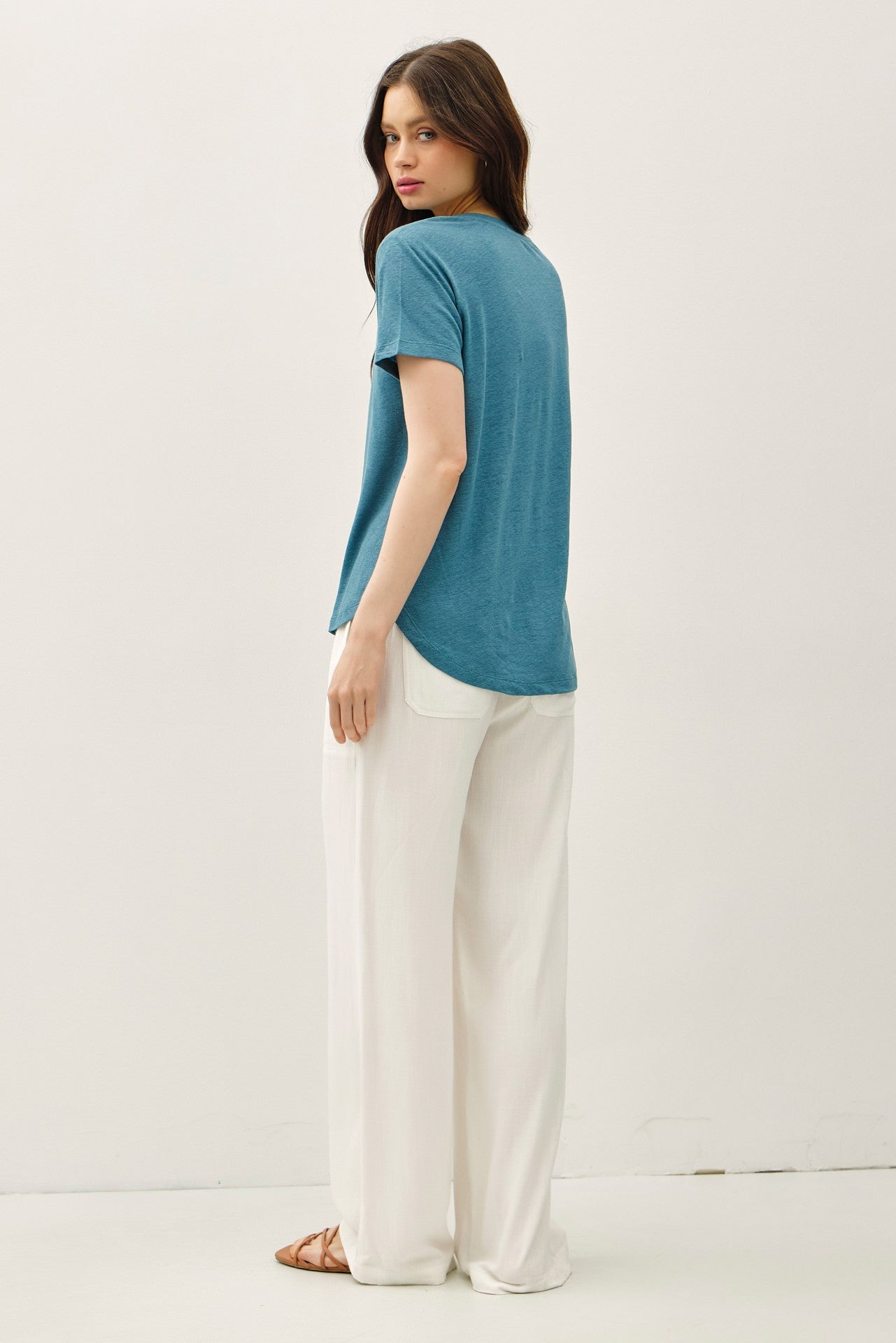 woman wearing a teal short sleeve top and white wide-leg pants, viewed from the back