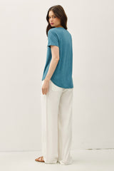 woman wearing a teal short sleeve top and white wide-leg pants, viewed from the back