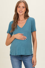 woman wearing a teal maternity top with a v-neckline and holding her baby bump