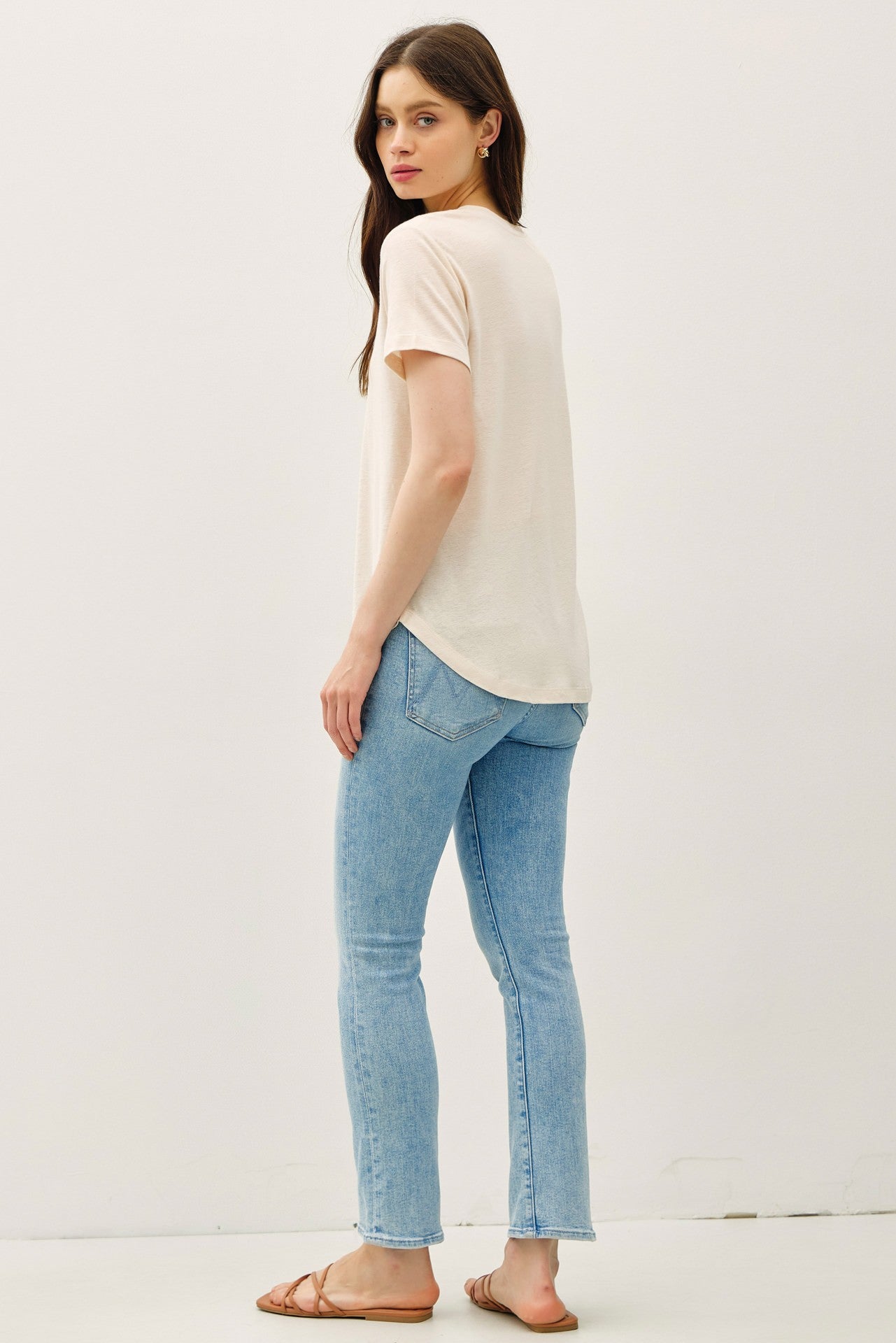 woman wearing a light beige short sleeve t-shirt and light blue skinny jeans, viewed from the back
