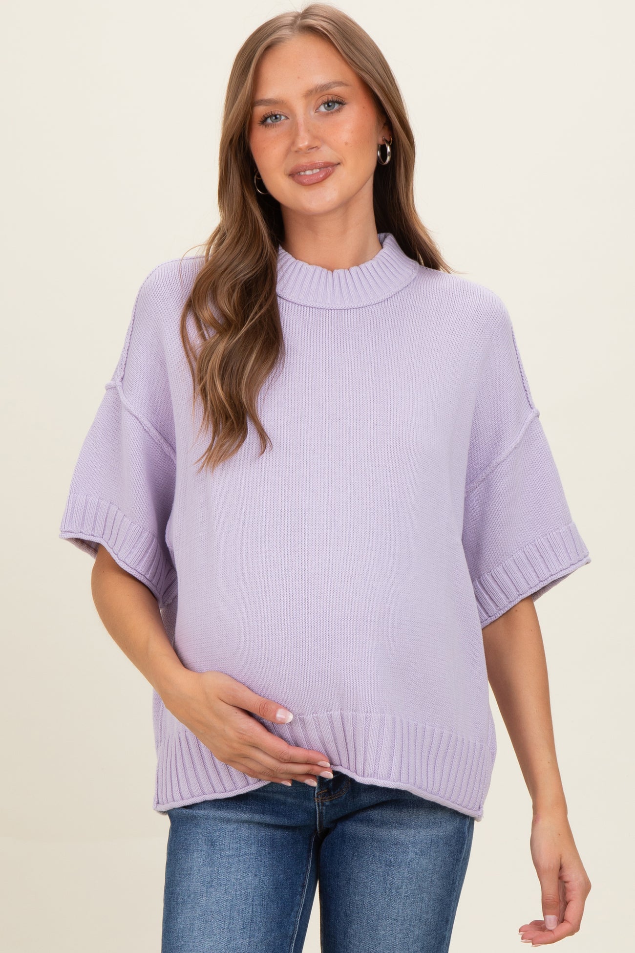 woman wearing a lilac maternity sweater with short sleeves and a ribbed hem, holding her baby bump