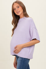 woman wearing a light purple short sleeve maternity sweater with a visible baby bump and casual blue jeans
