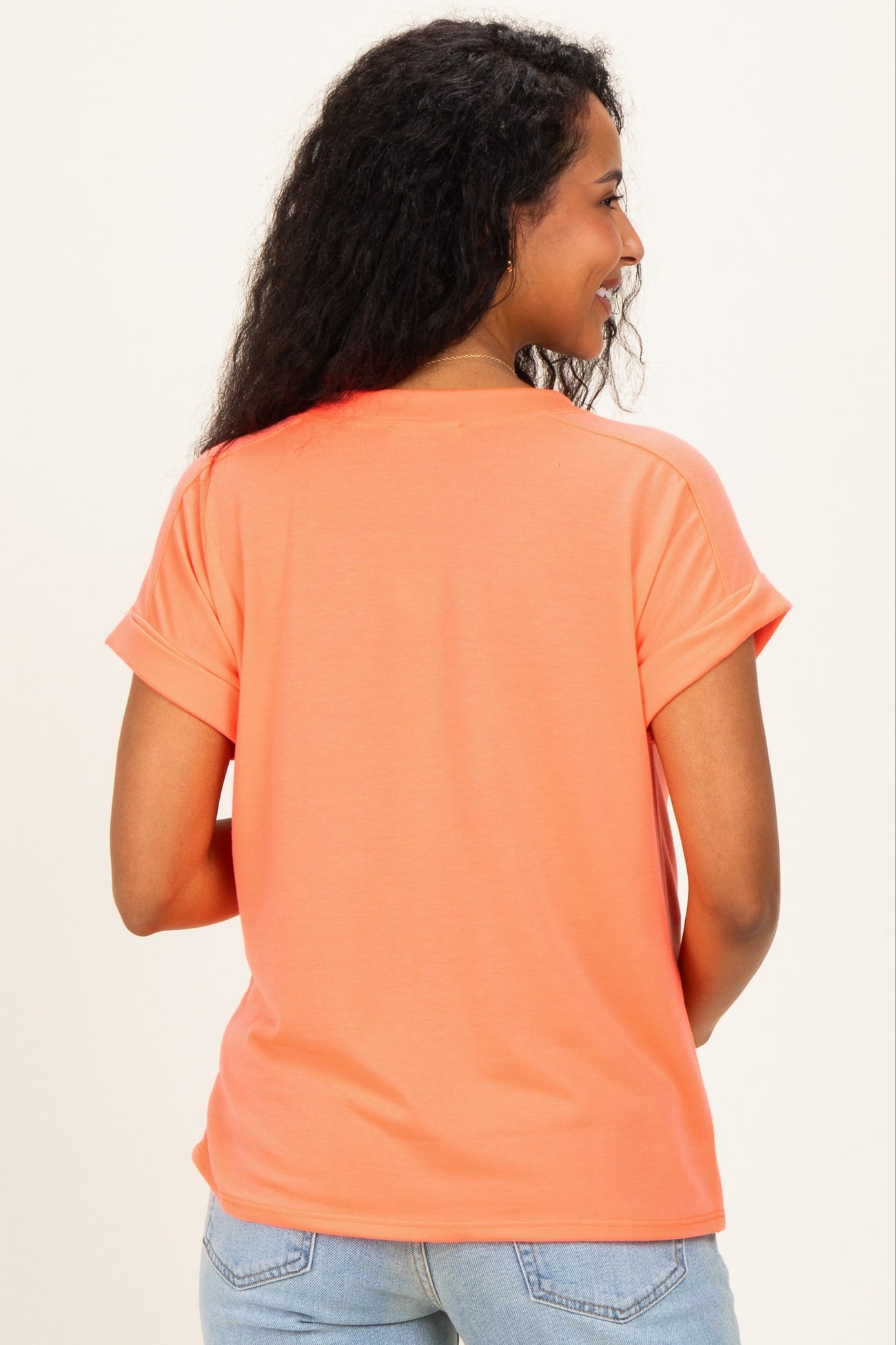 woman wearing a peach short sleeve maternity top, seen from the back, paired with light blue jeans