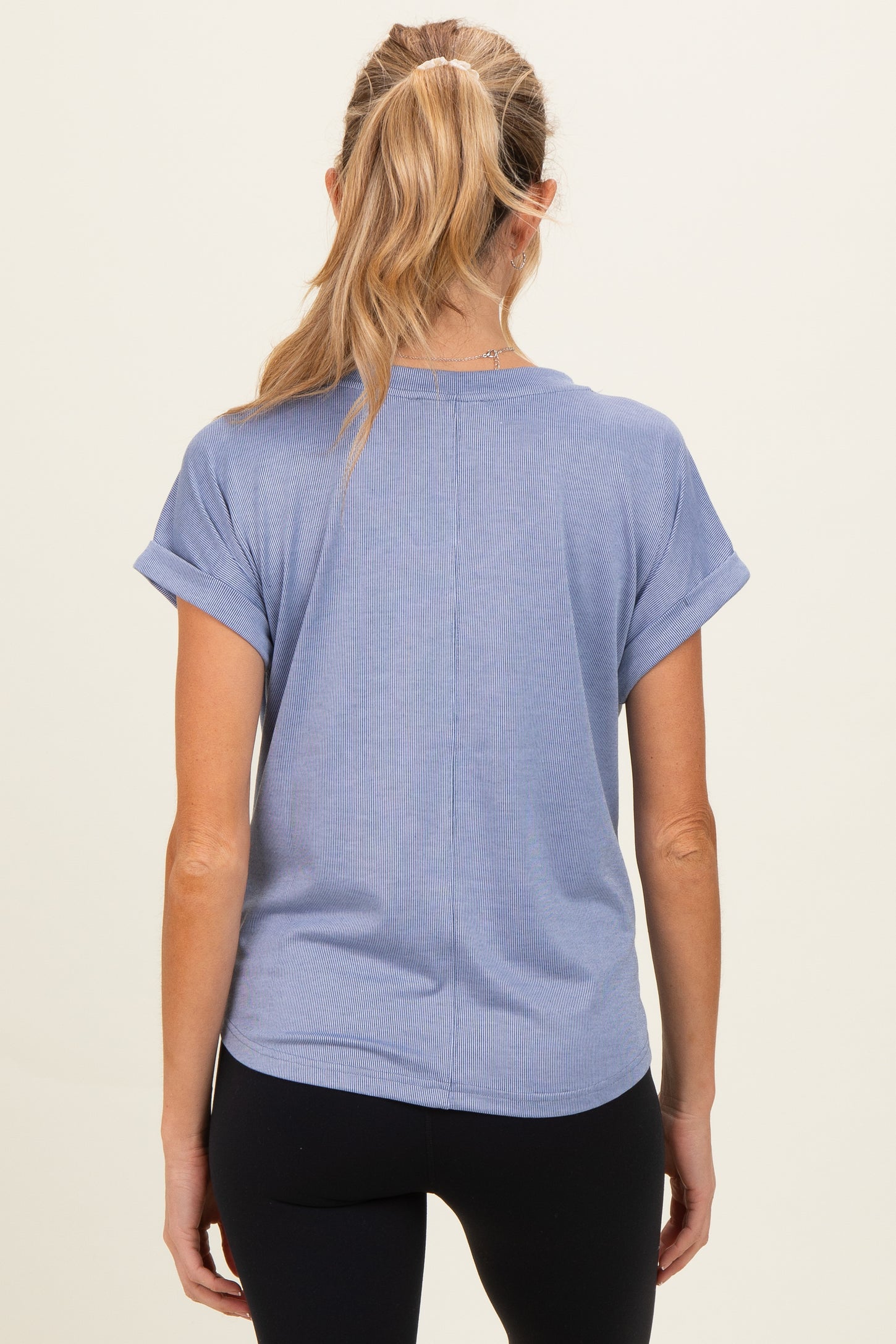 woman wearing a light blue maternity short sleeve top, viewed from the back, styled with rolled cuffs