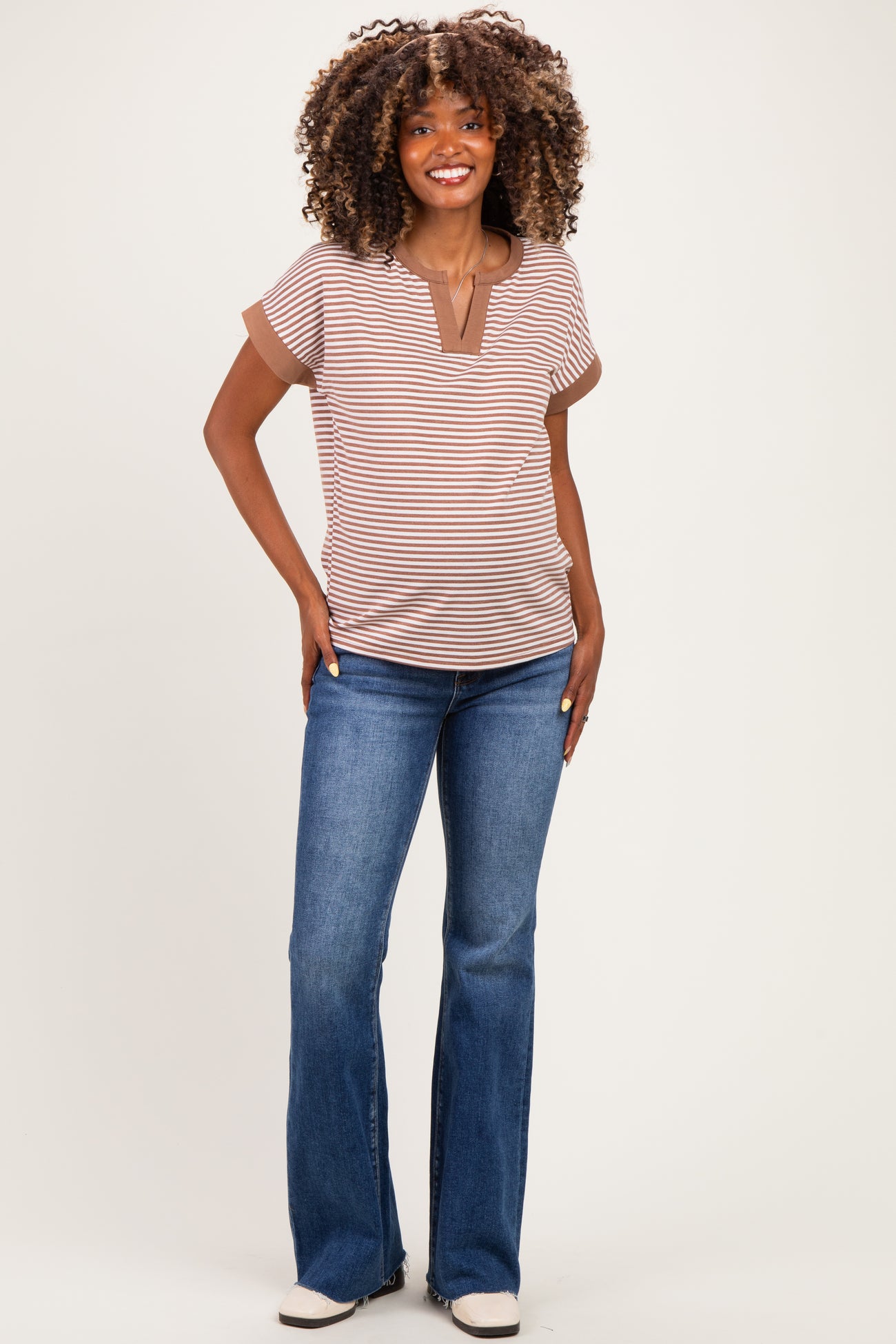 woman wearing a brown and white striped maternity top with a v-neck and flared jeans, showcasing her baby bump
