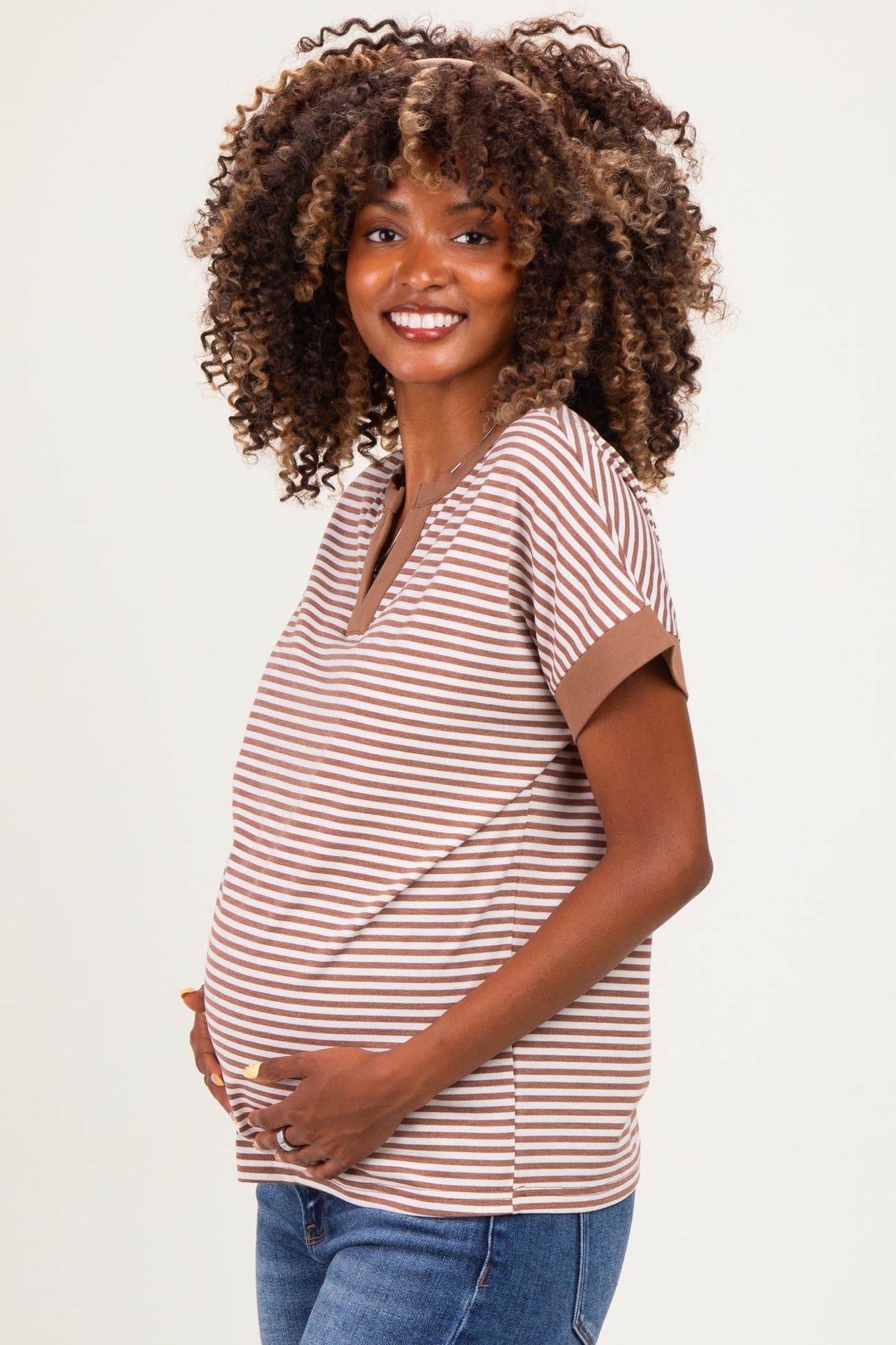woman wearing a striped brown and cream maternity top, gently cradling her baby bump