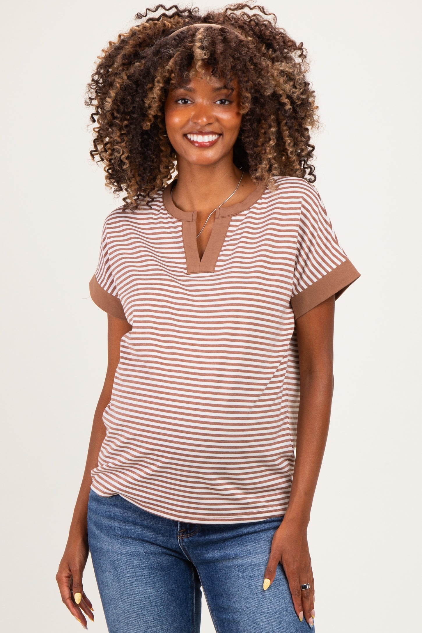 woman wearing a brown and beige striped maternity top with a slight v-neck and short sleeves, smiling at the camera