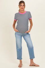 woman wearing a black and white striped maternity top with pink accents and light blue jeans, hands in pockets
