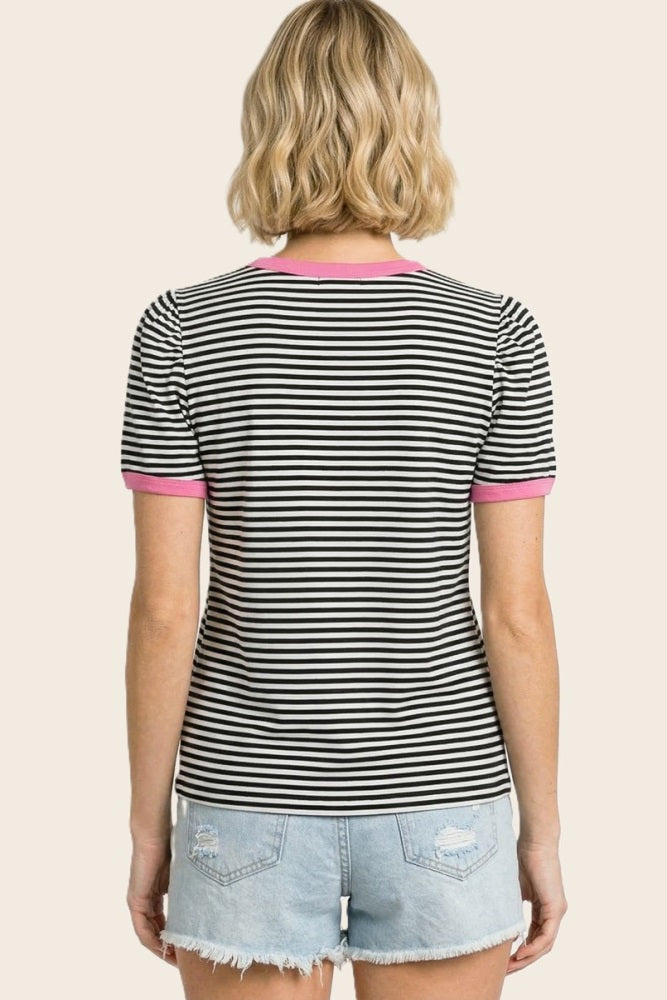 woman wearing a black and white striped short sleeve shirt with pink trim, facing away, paired with denim shorts