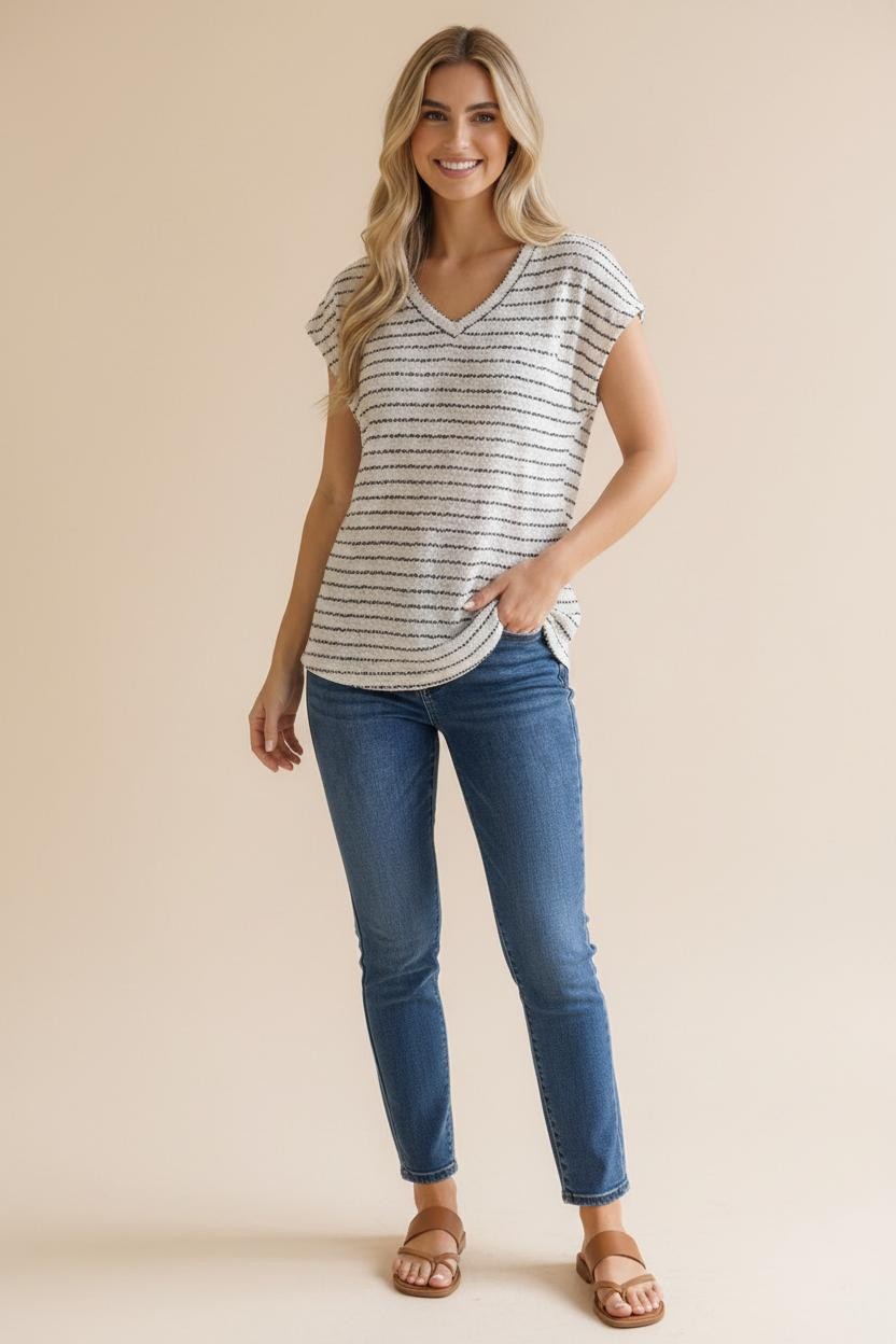 woman wearing a light gray striped short sleeve v-neck top and blue skinny jeans, standing with one hand in her pocket