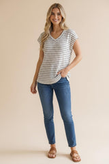 woman wearing a light gray striped short sleeve v-neck top and blue skinny jeans, standing with one hand in her pocket