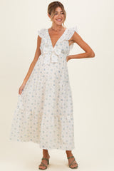 woman wearing a white floral print maternity maxi dress with ruffled sleeves and a bow detail at the neckline, showing her baby bump