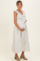 woman wearing a white floral maternity dress with ruffled sleeves and a tie detail, holding her baby bump