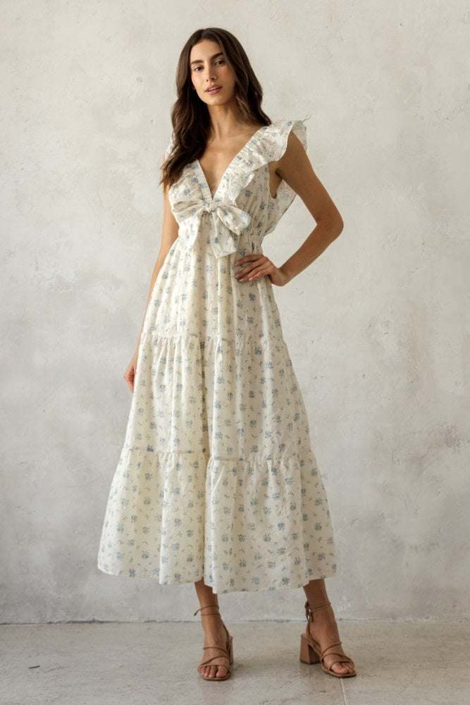 woman wearing a cream floral maxi dress with ruffled sleeves and a tie-front detail