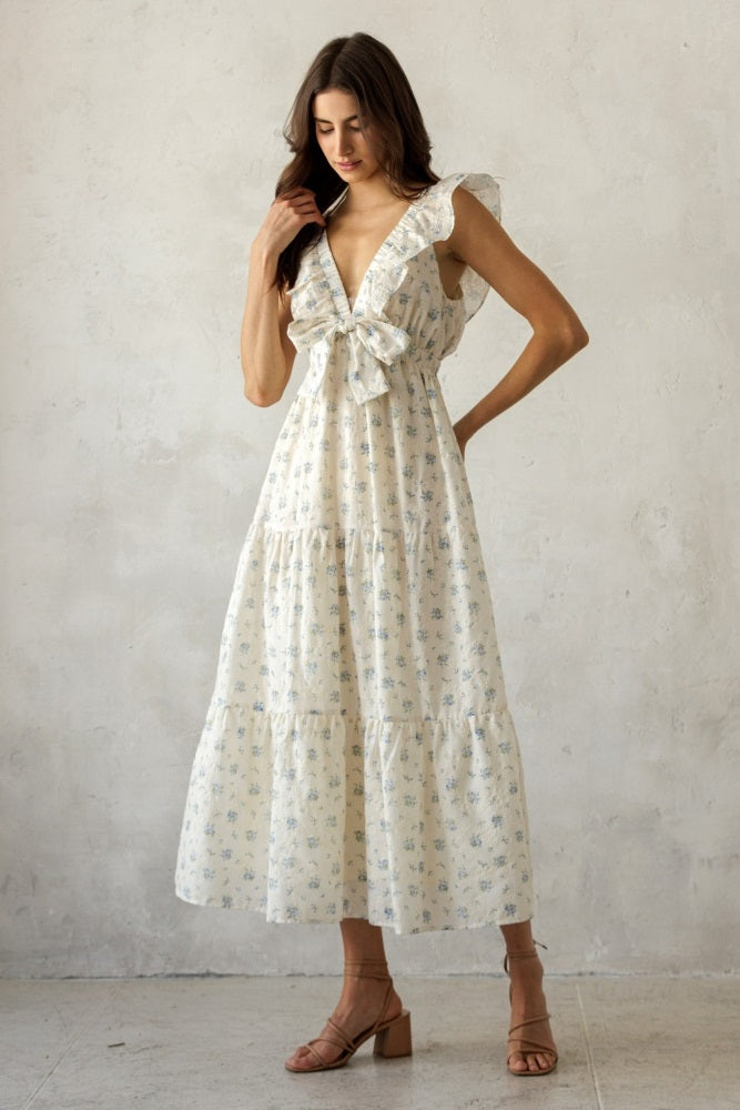 woman wearing a white floral maxi dress with ruffle sleeves and a tie detail at the waist