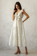 woman wearing a white floral maxi dress with ruffle sleeves and a tie detail at the waist