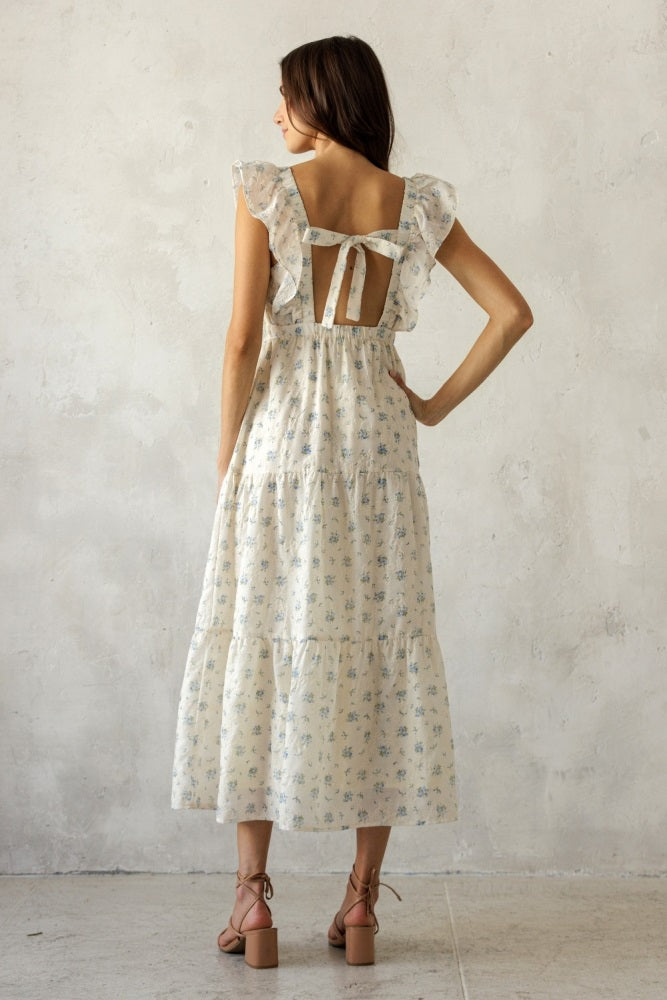 woman wearing a floral print midi dress with ruffle sleeves and an open back, facing away from the camera