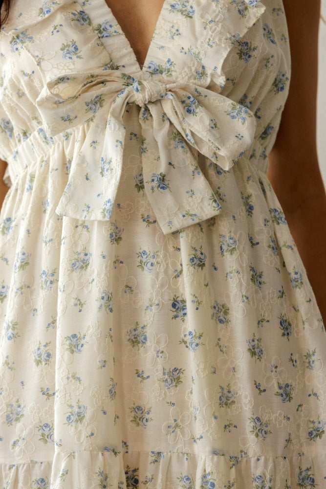 woman wearing a cream floral dress with a deep v-neck and bow detail on the bodice