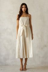 woman wearing a cream-colored spaghetti strap midi dress with a belted waist and a flowing skirt