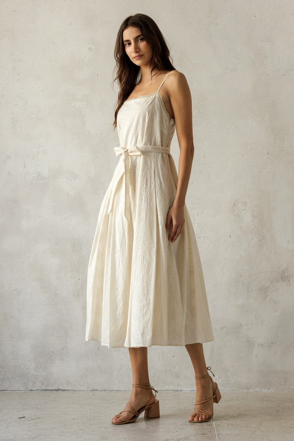 woman wearing an off-white sleeveless midi dress with a belted waist and full skirt, styled with tan block-heel sandals