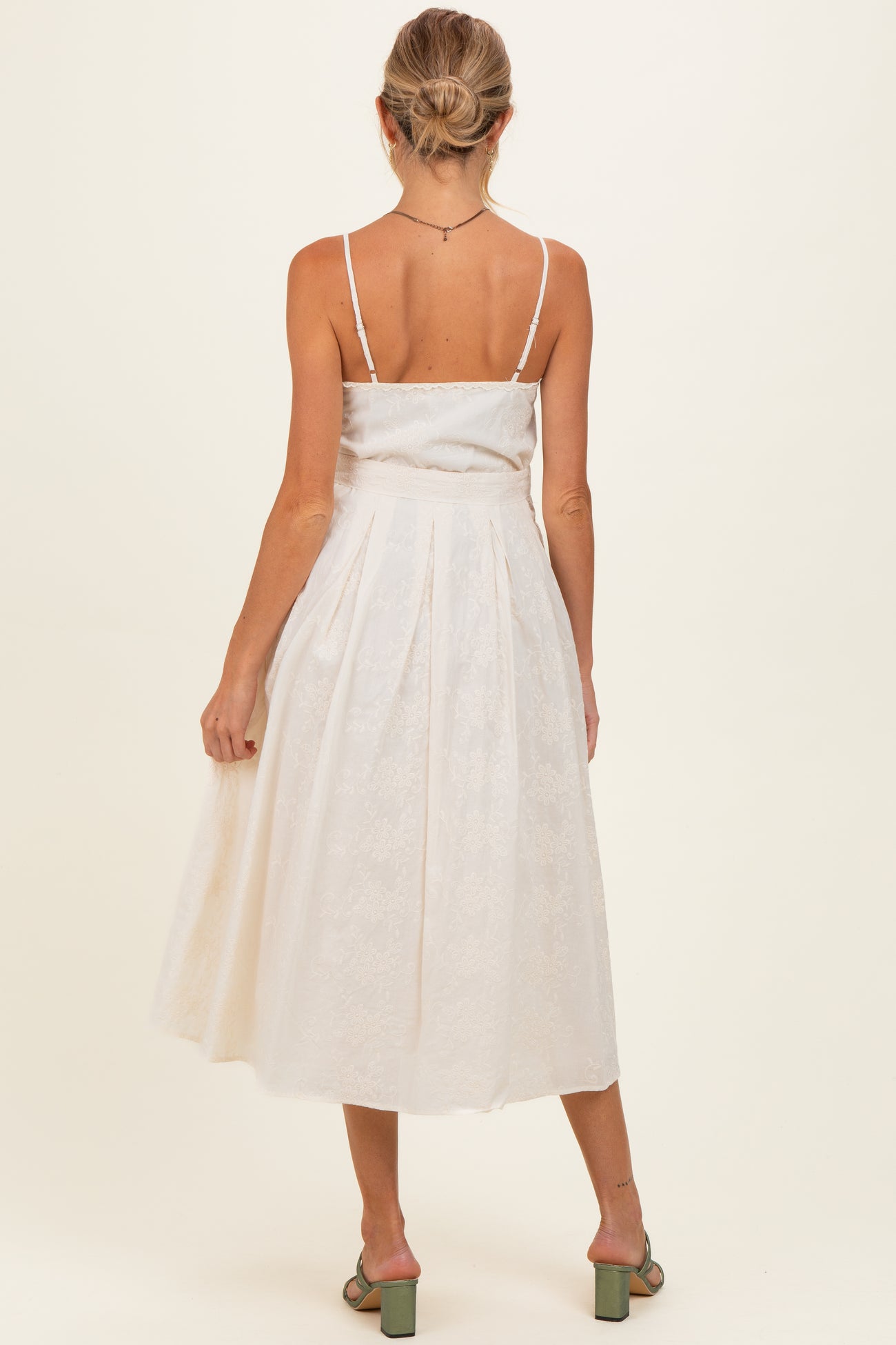 woman wearing a white sleeveless maternity dress with a pleated skirt, showing her back