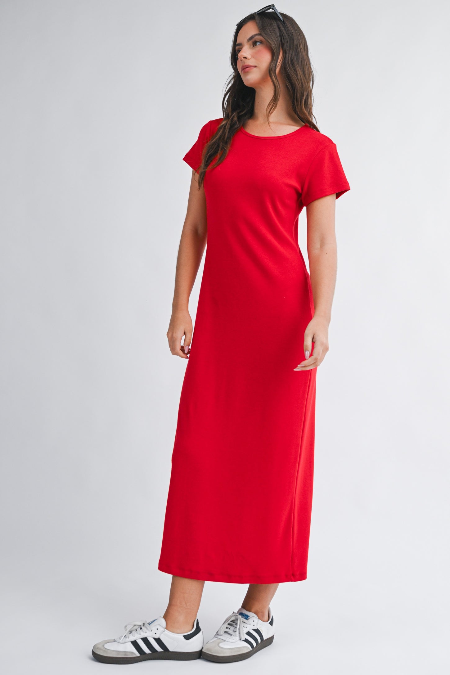 woman wearing a red short sleeve maxi dress and white sneakers, standing with one hand on her hip
