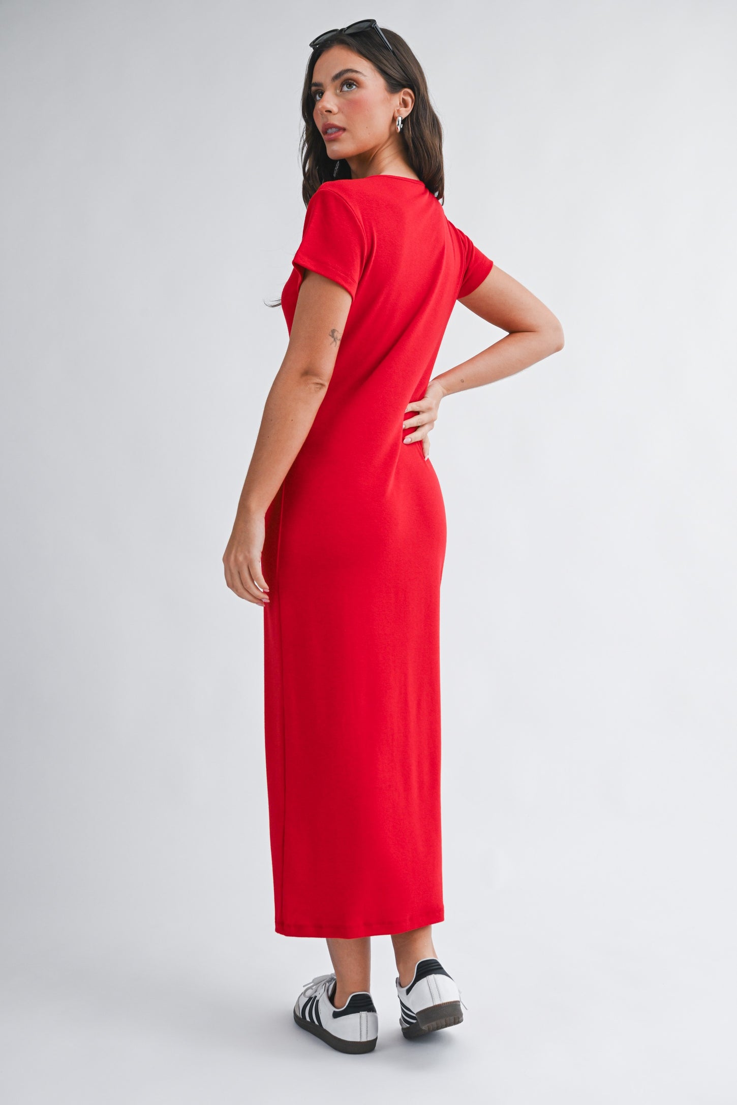 woman wearing a red short sleeve maxi dress and black and white sneakers, seen from the back