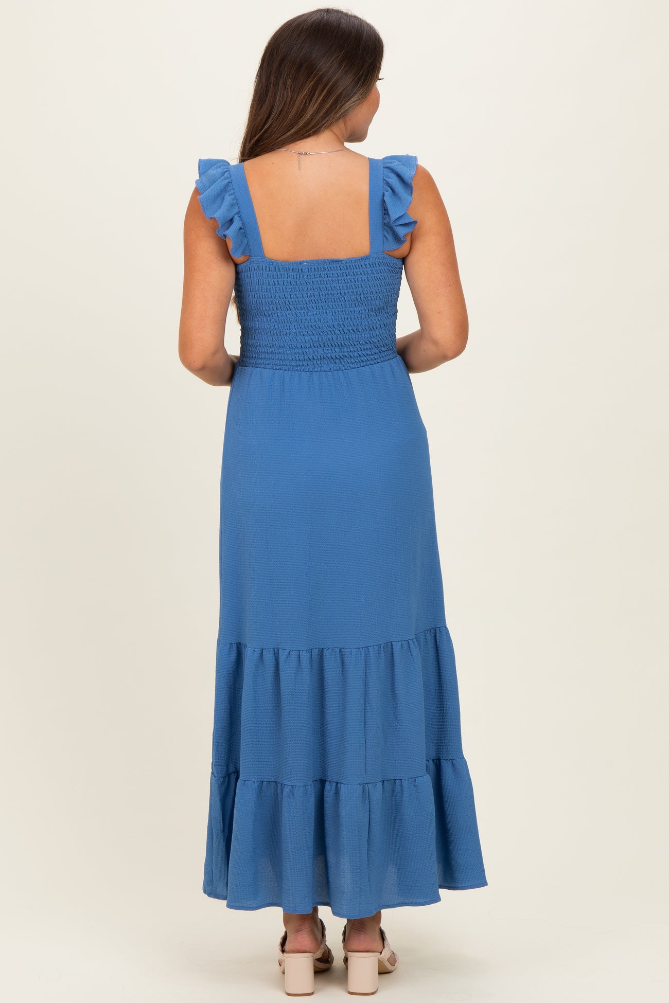 woman wearing a blue maternity maxi dress with ruffle straps and a tiered skirt, showing her back