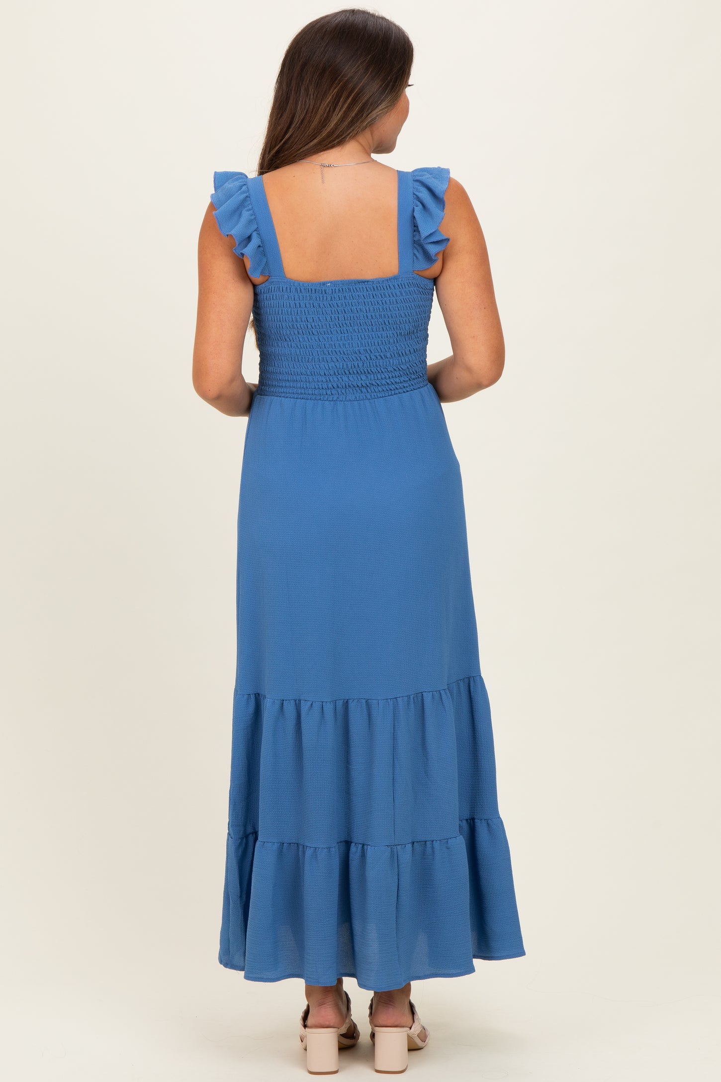 woman wearing a blue maternity maxi dress with ruffle straps and a tiered skirt, showing her back