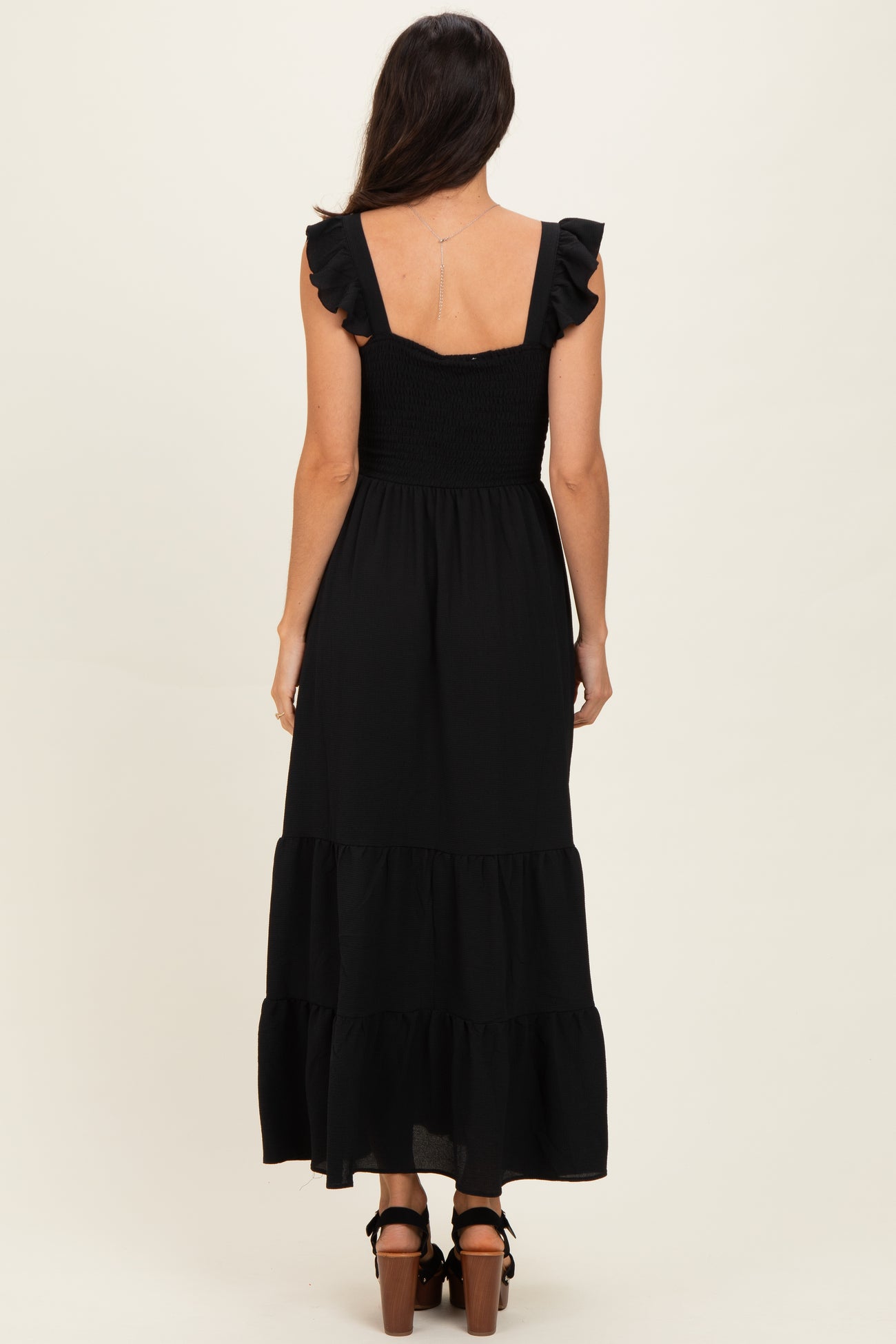 woman wearing a black maxi dress with ruffled straps and a smocked bodice, shown from the back