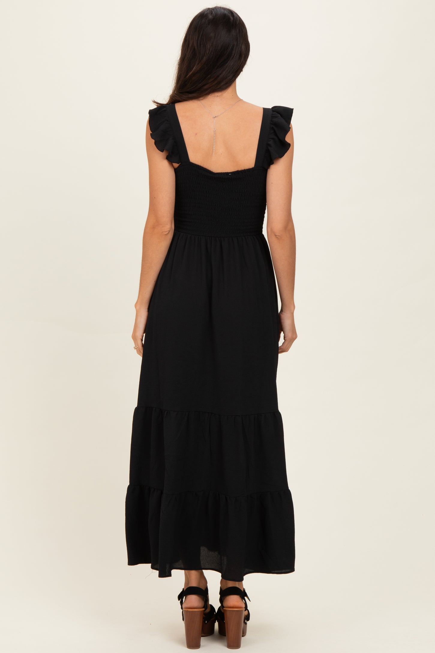 woman wearing a black maxi dress with ruffled straps and a smocked bodice, shown from the back