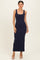 woman wearing a navy blue sleeveless maxi dress, posing with a neutral background and nude high heels
