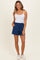 woman wearing a white tank top and denim blue shorts with side pockets