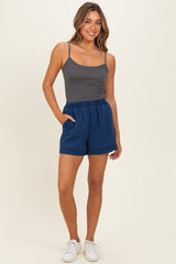 woman wearing a gray tank top and blue casual shorts, posing with hands in pockets