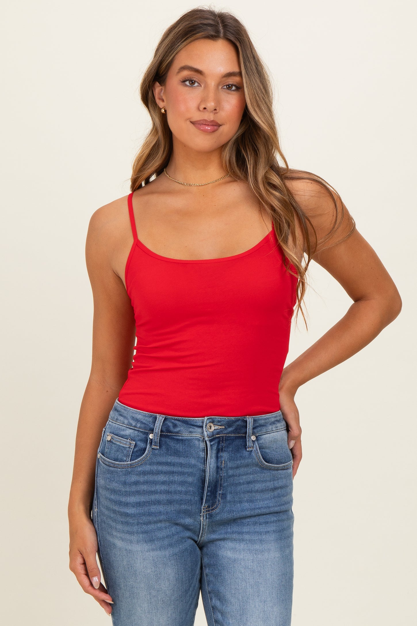 woman wearing a red fitted camisole top and blue high-waisted jeans