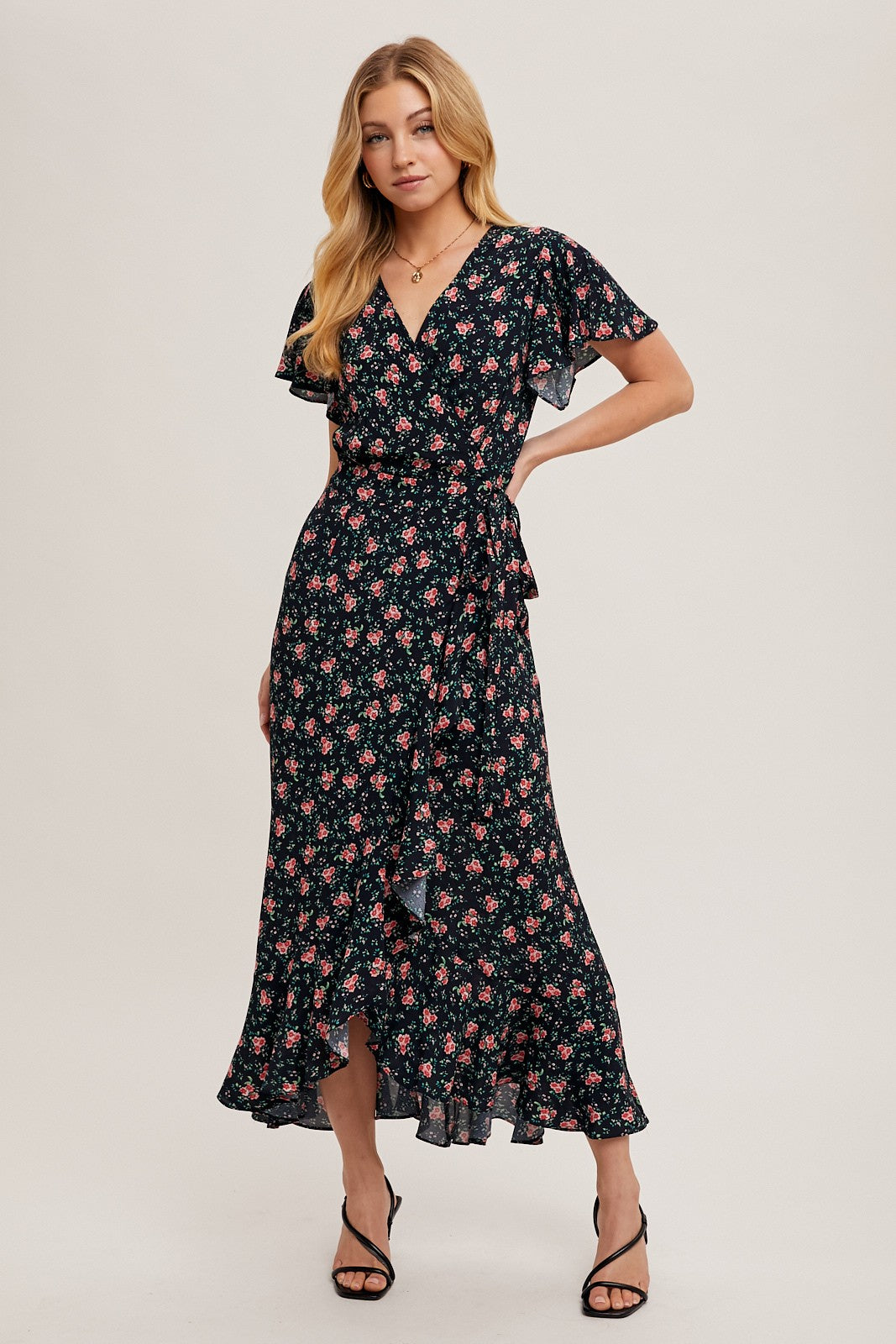 woman wearing a black floral wrap dress with ruffled sleeves and a high low hemline, standing confidently