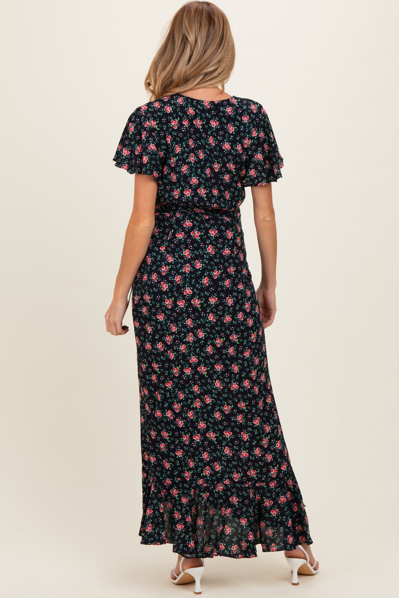 woman wearing a black floral maternity maxi dress with short flutter sleeves and a ruffled hem