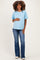 woman wearing a light blue maternity t-shirt and blue flared jeans, gently holding her baby bump