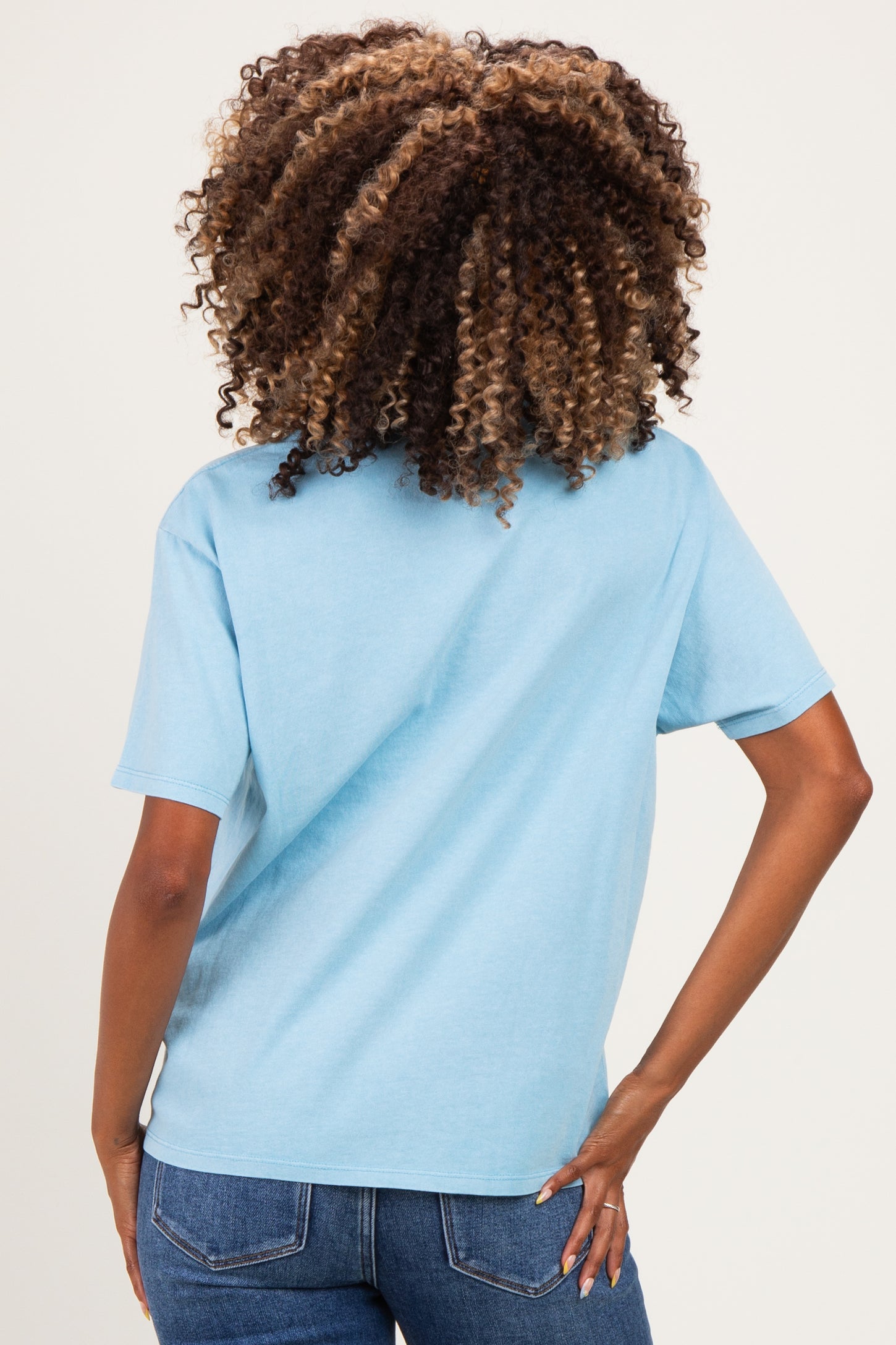 woman wearing a light blue short sleeve maternity top, view from the back, with curly hair and casual denim jeans