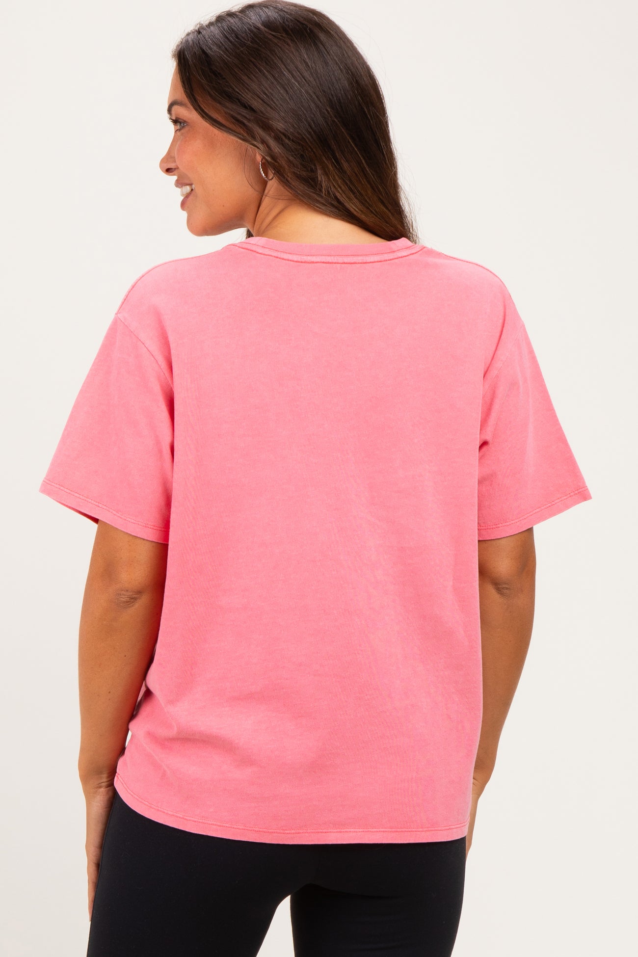 woman wearing a pink oversized maternity t-shirt, shown from the back, paired with black leggings