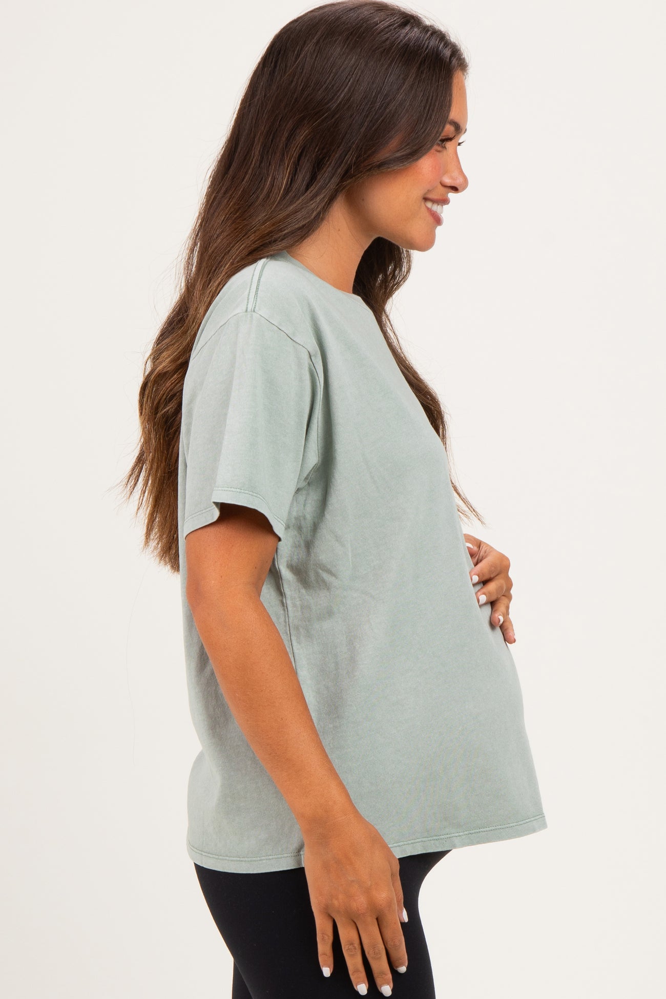 woman wearing a faded green maternity t-shirt and holding her baby bump from the side