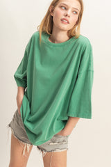 woman wearing an oversized green t-shirt and distressed gray shorts, posing with hands in pockets